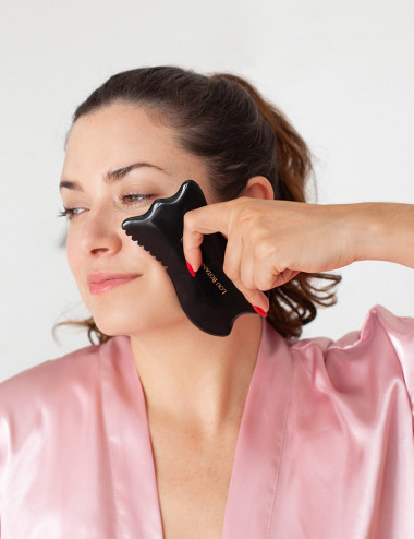 Mujer usando gua sha tulip cuarzo bian negro para masaje facial